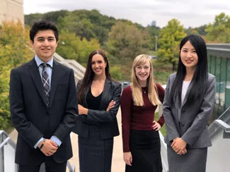Four students in business attire posing outdoors at UTM campus